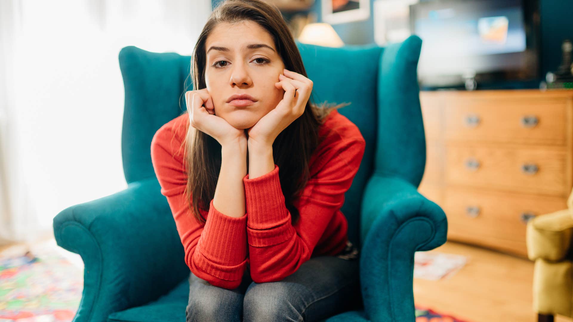 Young woman looks seriously at the couch in a wingback chair 