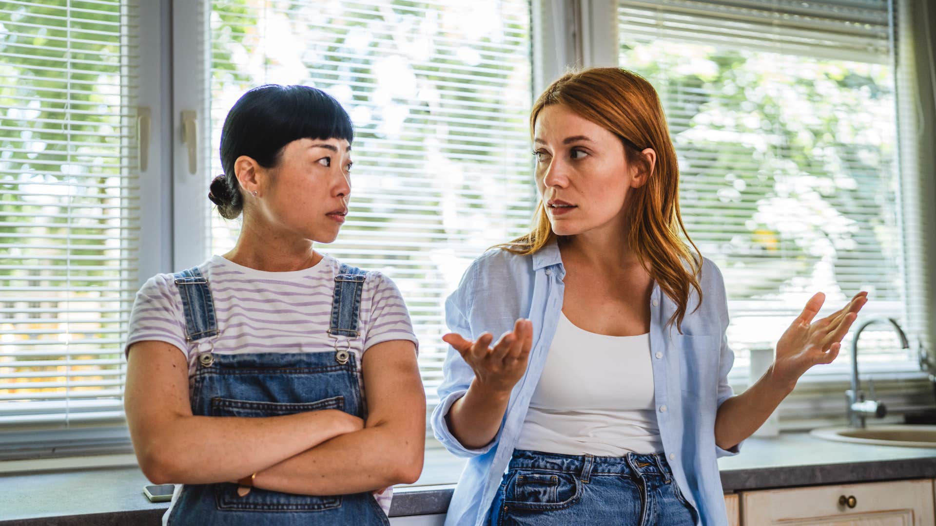 friends talking seriously by window as one friend with blonde hair says gosh i was just joking