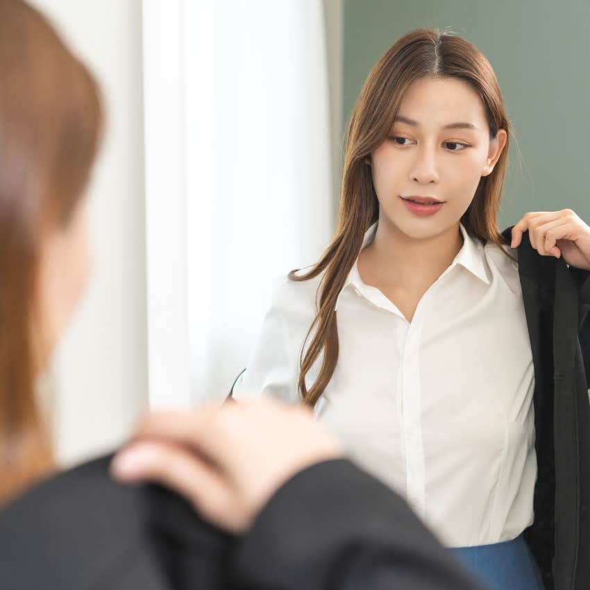 businesswoman getting dressed for work putting on blazer in mirror