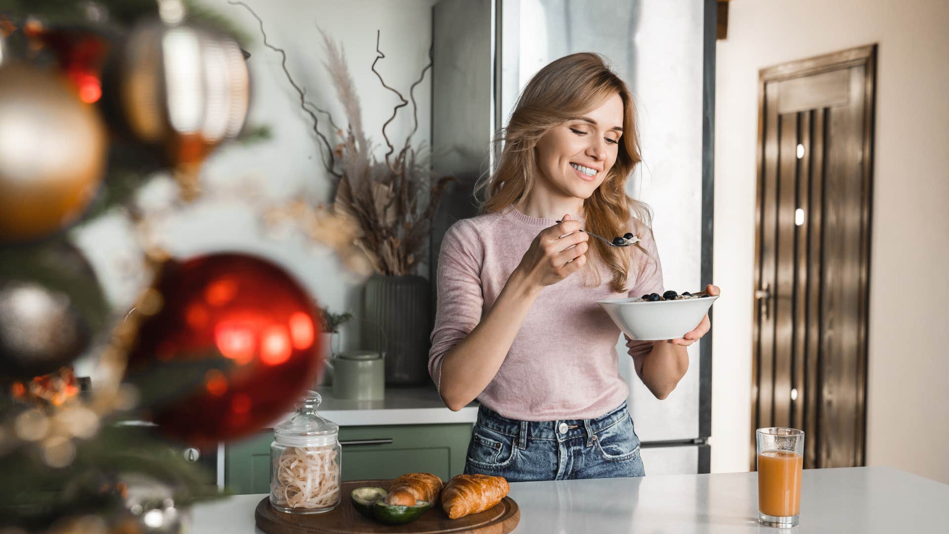 american woman eating in kitchen with christmas decorations
