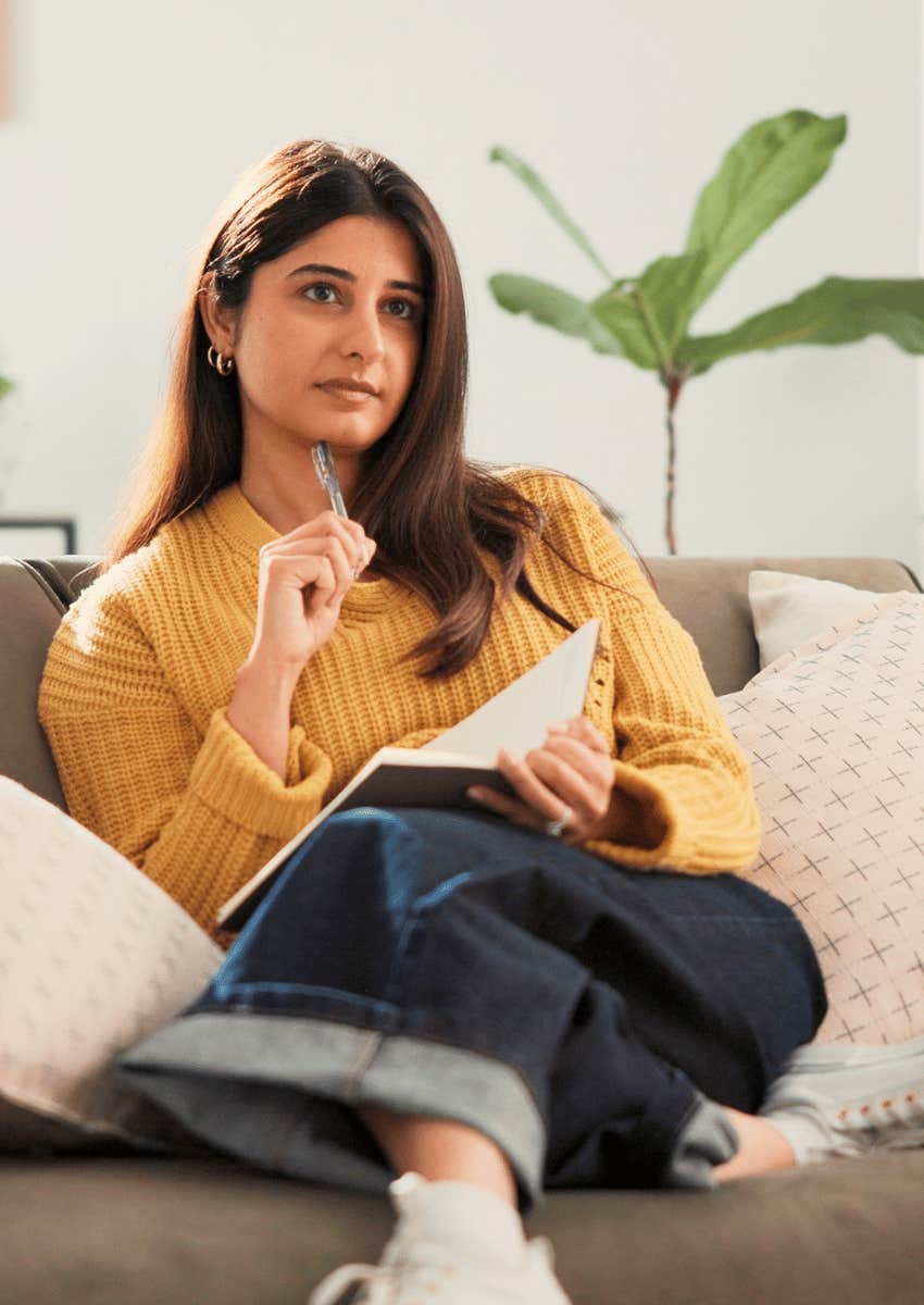 thoughtful woman sitting alone writing in her journal