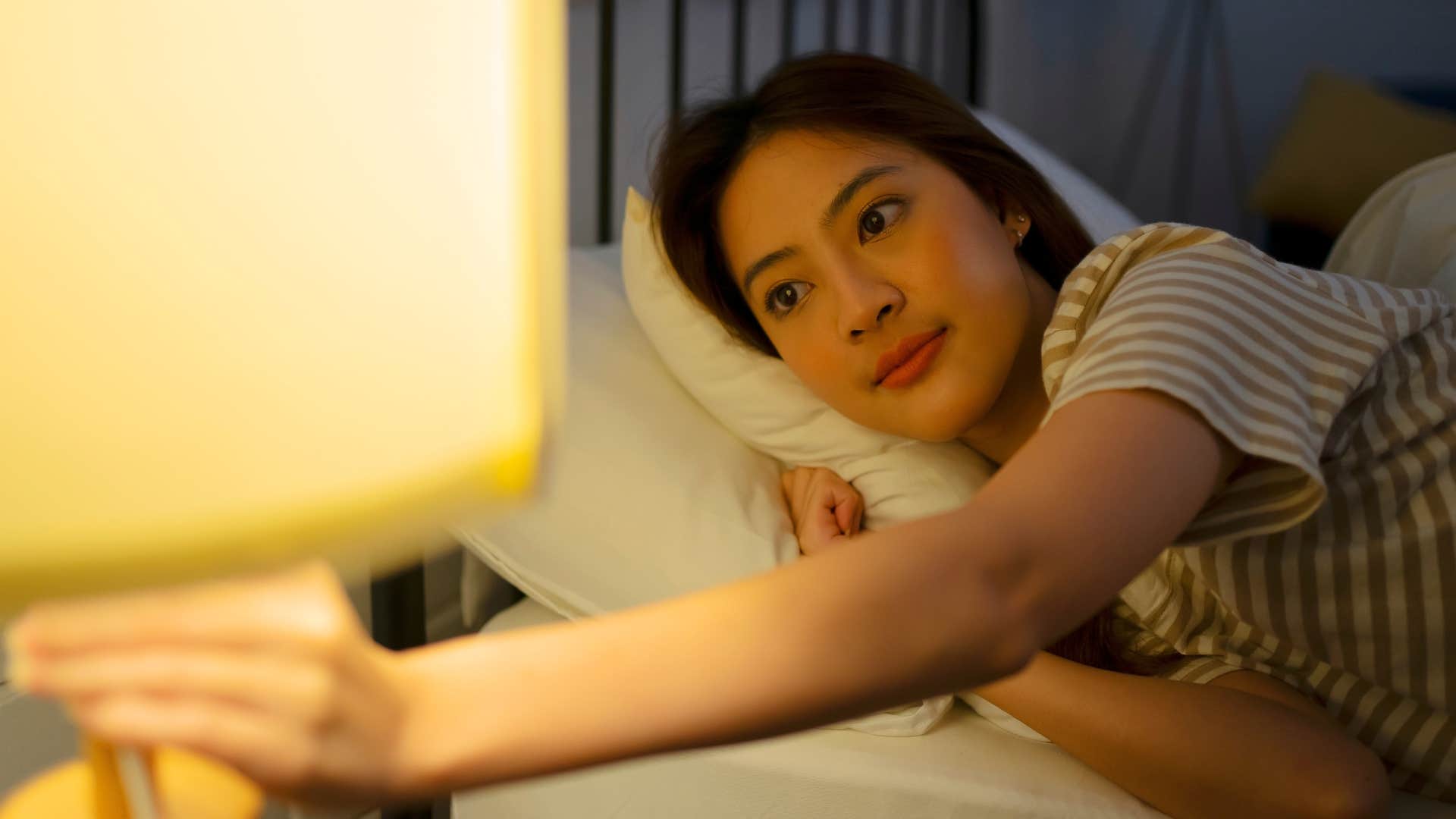 woman prioritizing sleep turning off lamp in bed