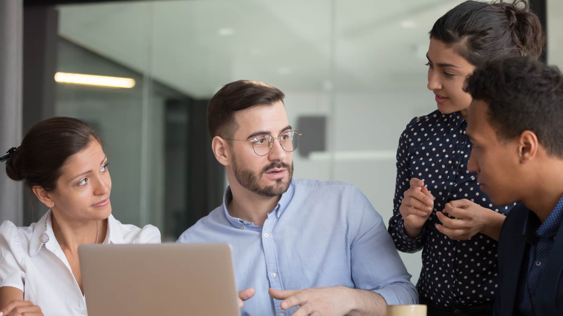 coworkers in group meeting as man in blue asks for feedback from everyone
