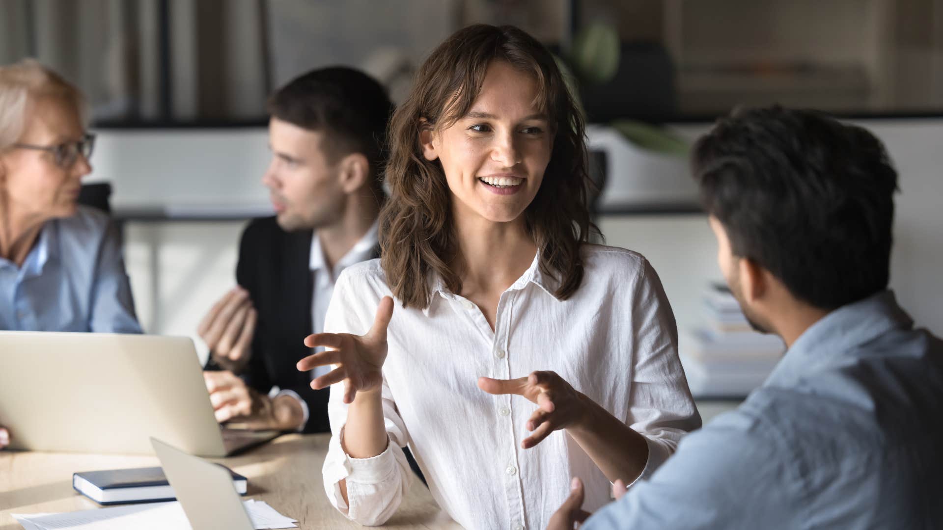 coworkers chatting at meeting as woman in white shirt asks more questions than they answer