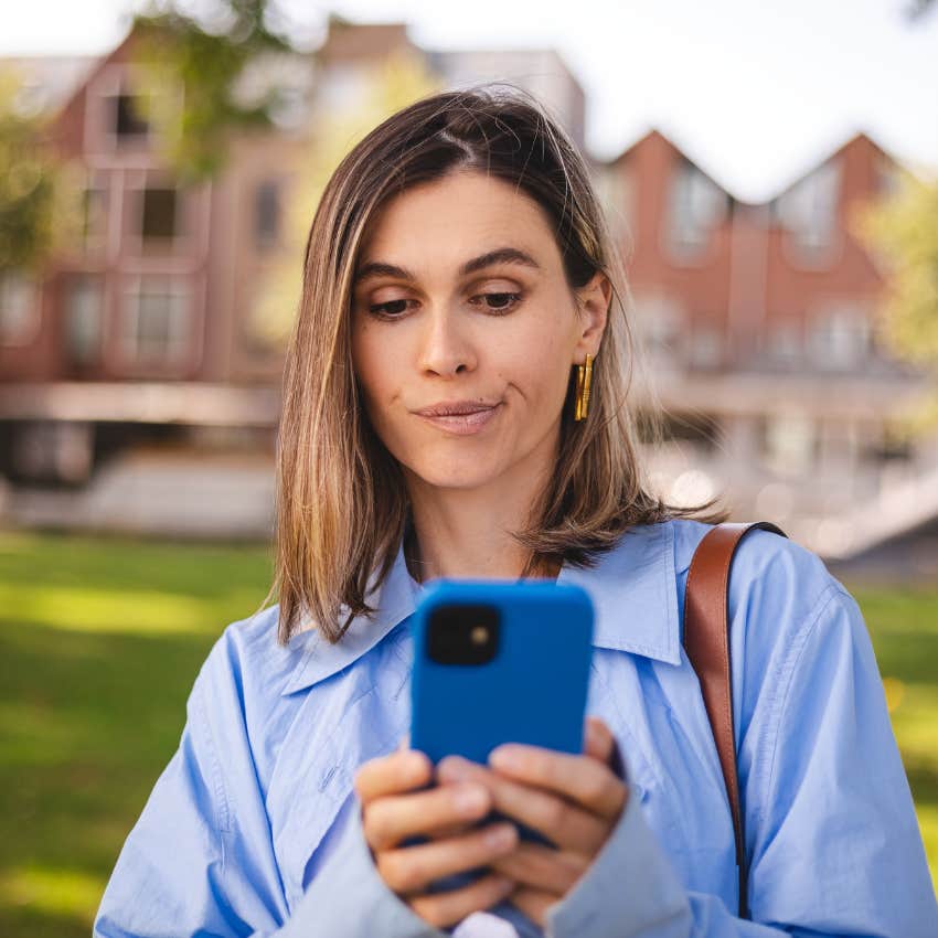 unimpressed woman looking at her phone while standing outside