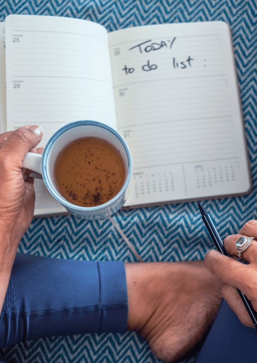 woman holding a cup of tea and writing a to-do list