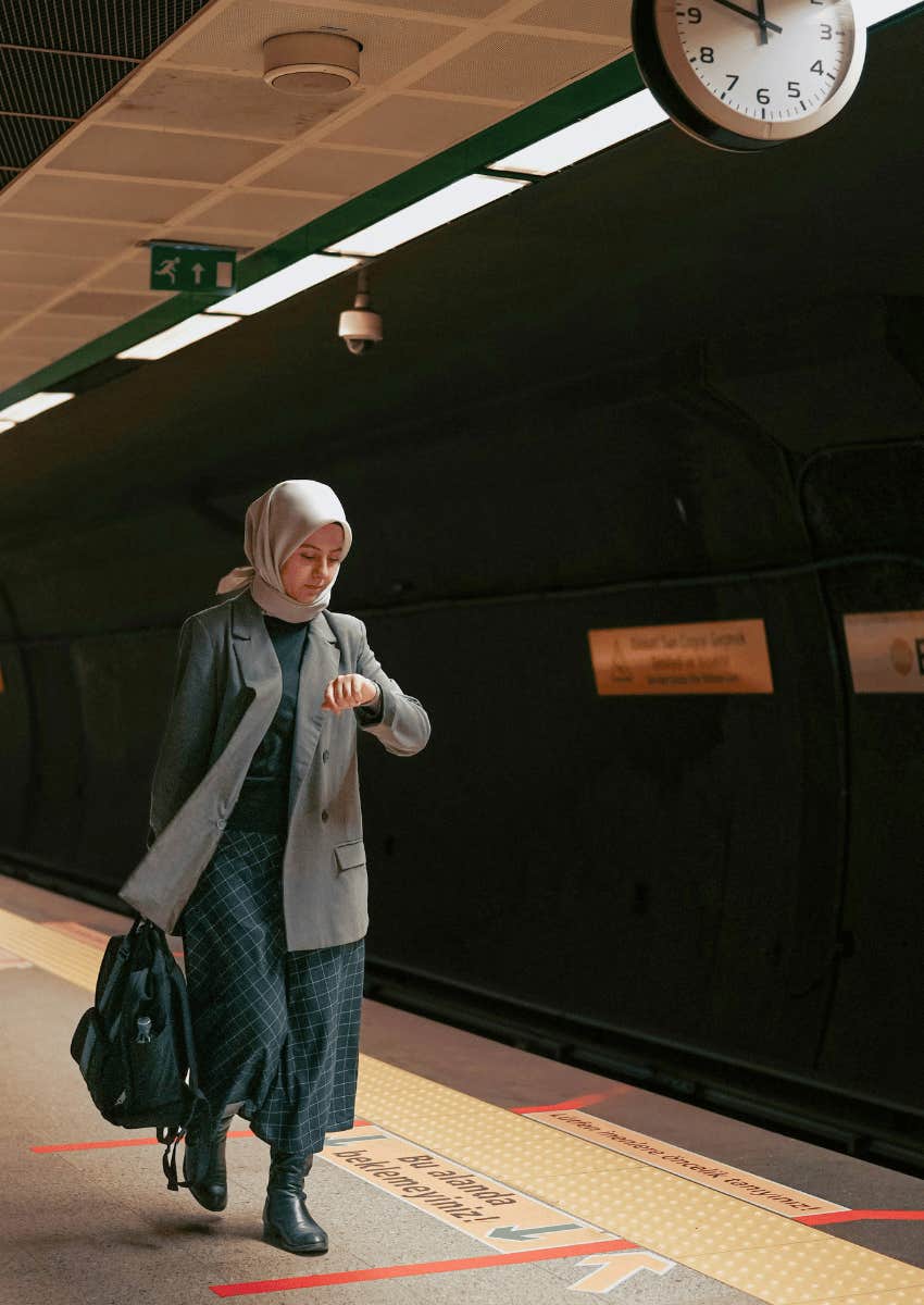woman looking down at her watch walking through train station