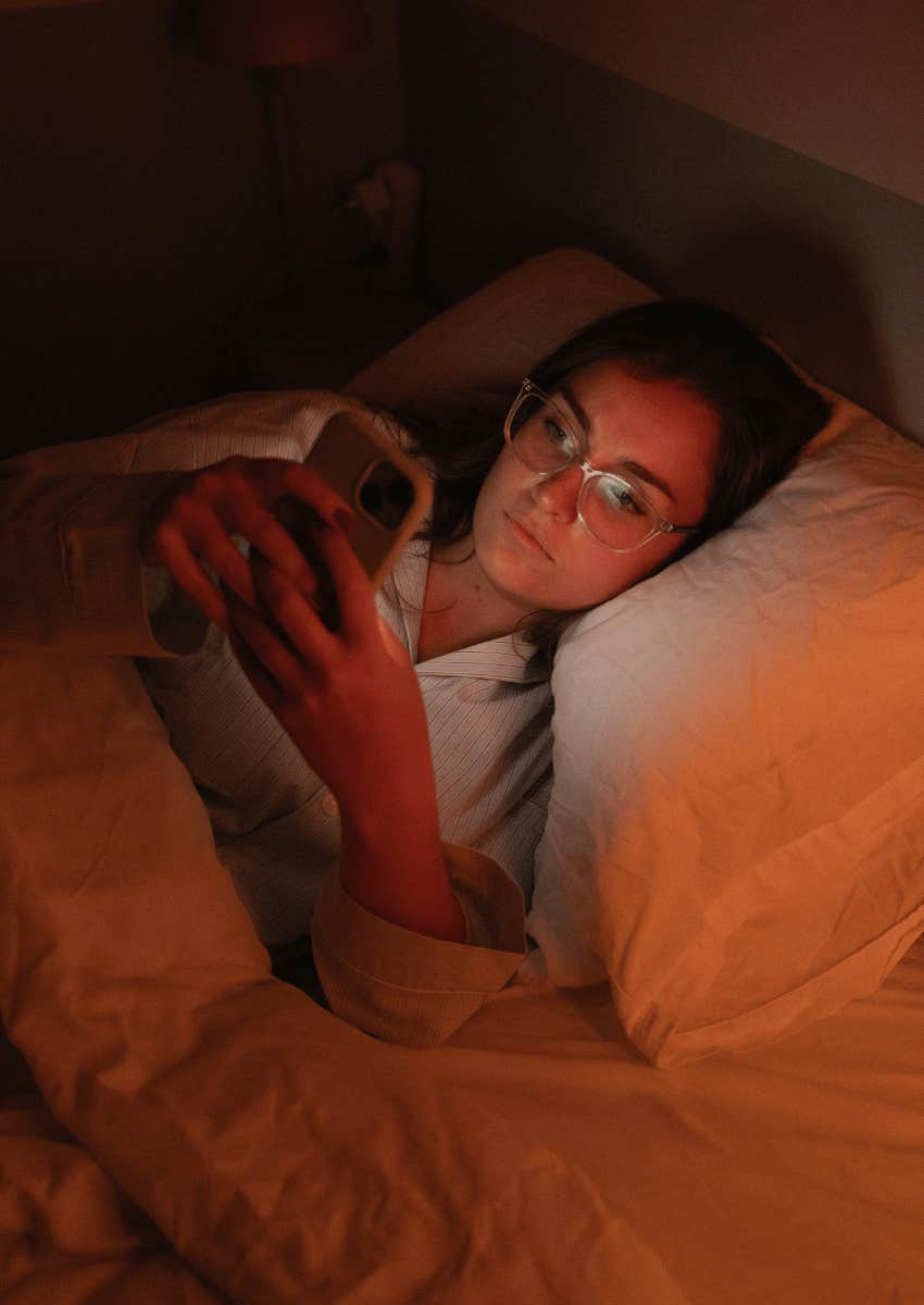 woman scrolling through her phone while laying in bed