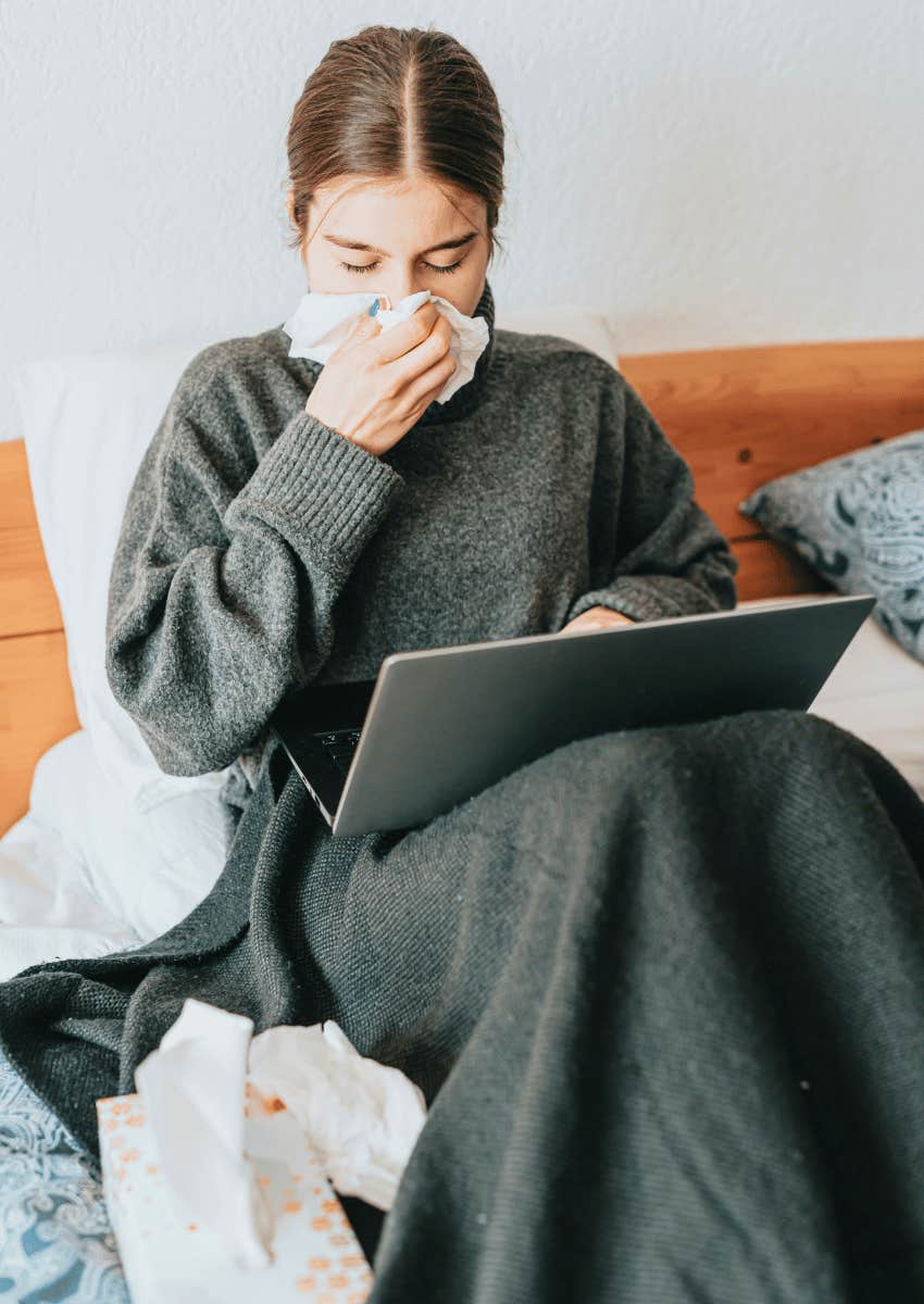 woman sick at home in bed working on laptop