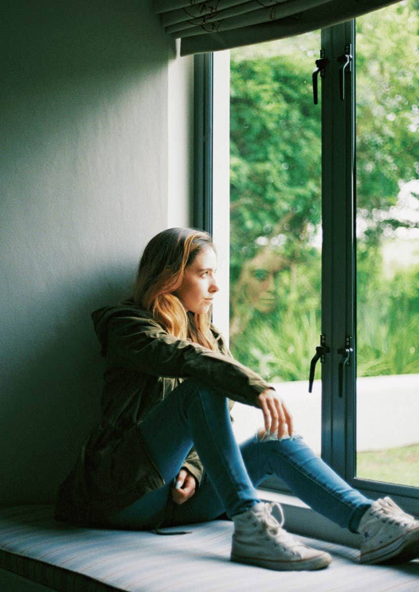 woman sitting on window looking out thoughtful