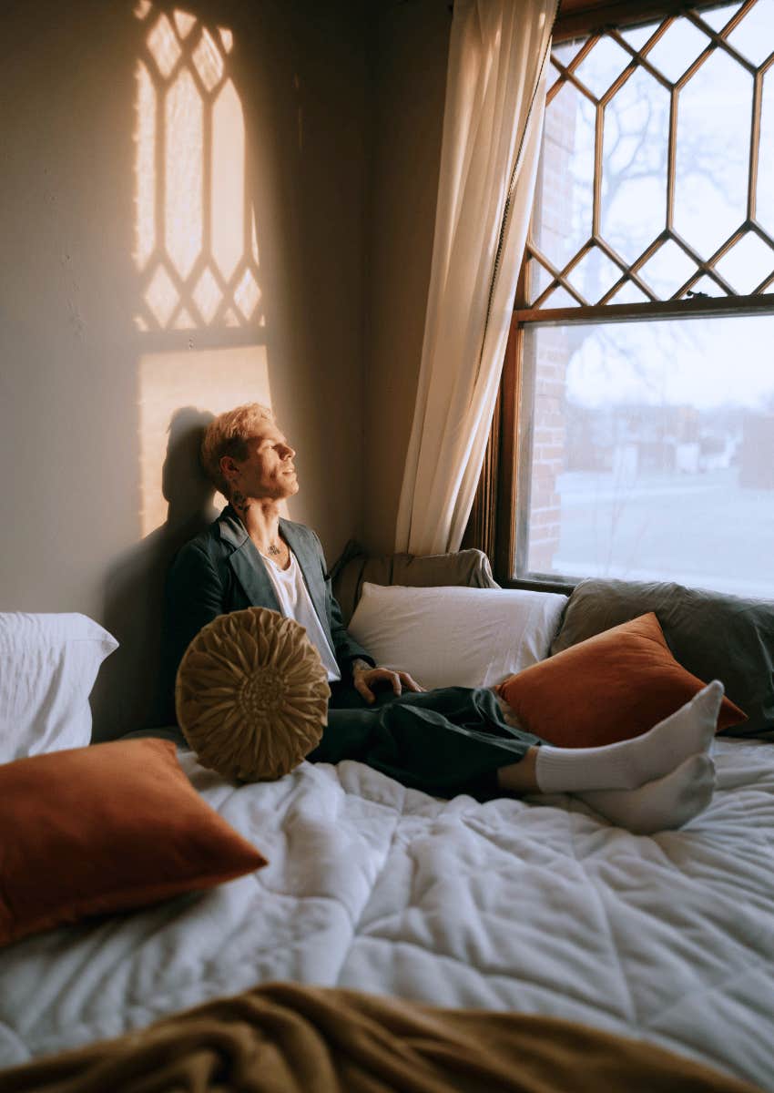 young man sitting alone in bed looking out of window