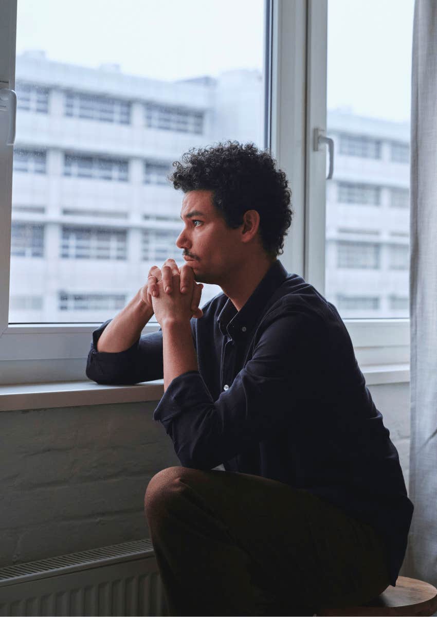 thoughtful young man sitting alone by window
