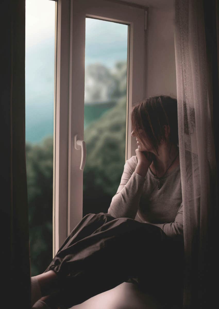 young woman sitting alone looking out of window