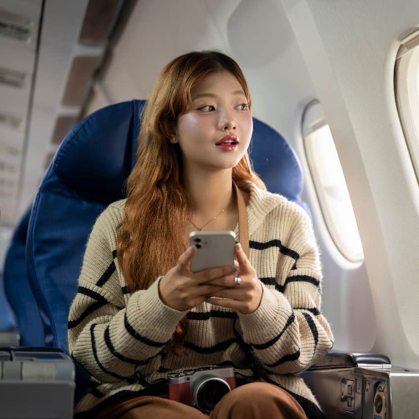 woman sitting in plane seat looking out window and holding smartphone