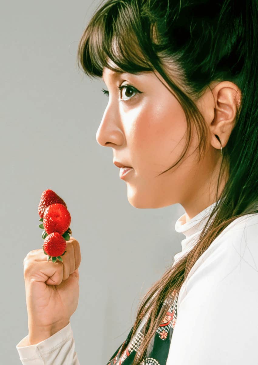brunette woman holding strawberries in a closed fist