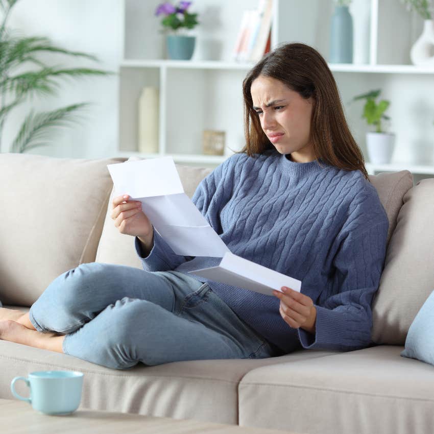 confused woman sitting on couch reading hospital bill
