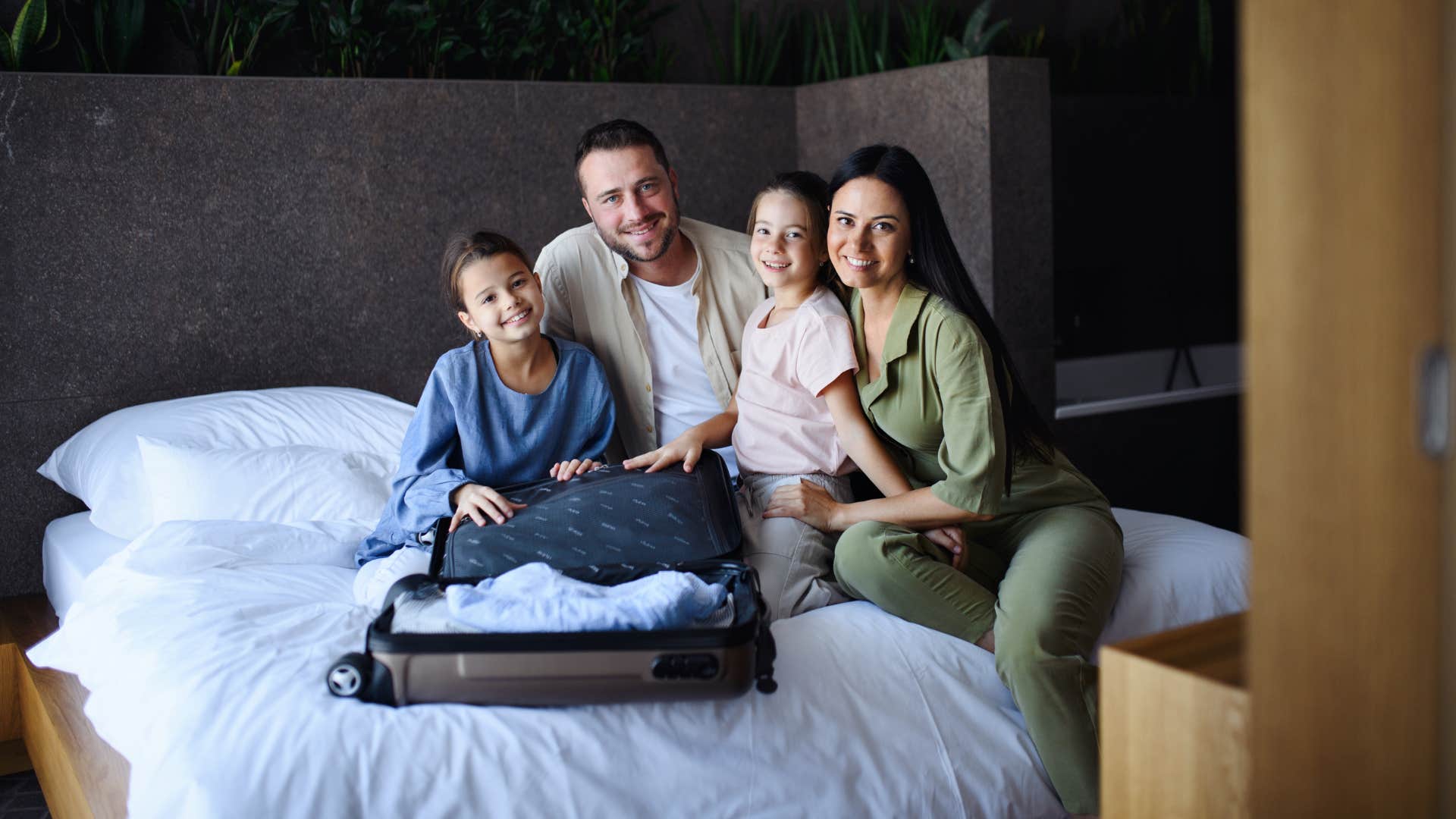 family with kids in a hotel bed unpacking their suitcase for vacation