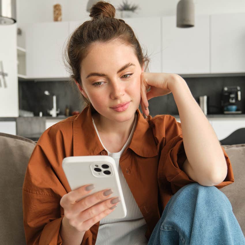 young woman using smartphone resting hand on face would rather stay home than go out like her mom did
