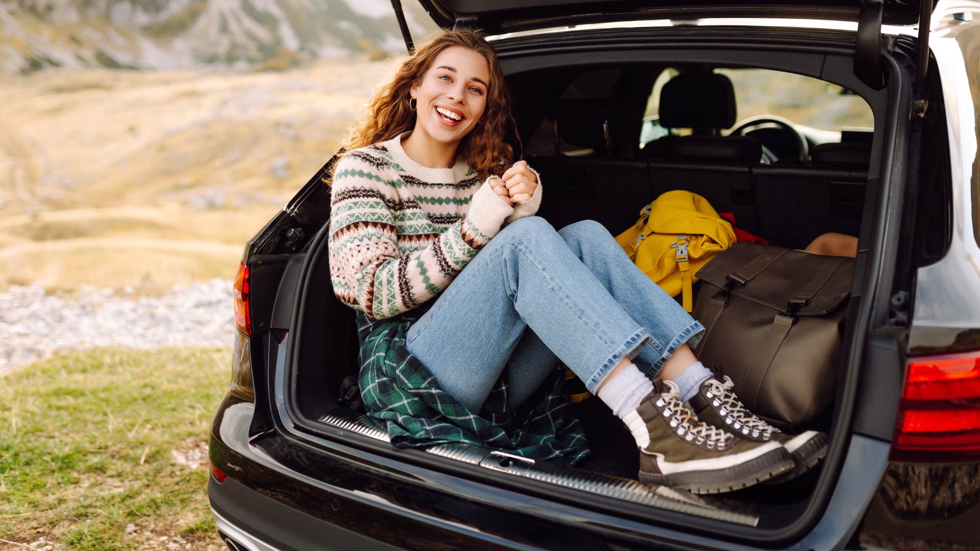 woman sitting in trunk of car on a road trip instead of spending money on material items