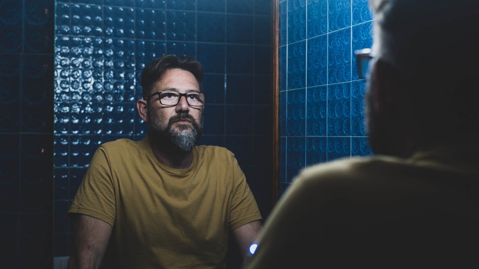 stressed man looking in the mirror not showing himself compassion