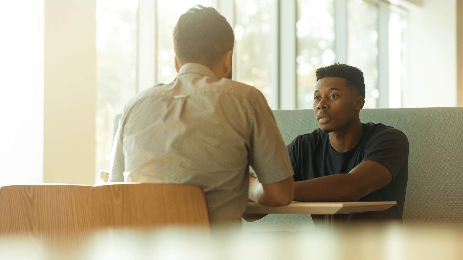 man sitting at a booth not trusting his partner beside him