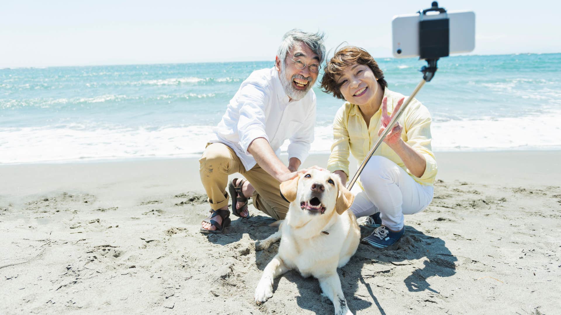 older couple on a beach taking a selfie with their dog to post online