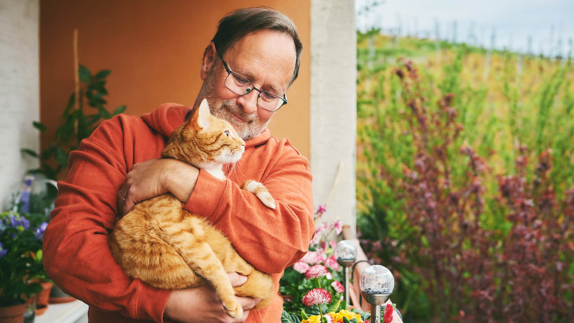 older gentleman holding his cat on a balcony smiling