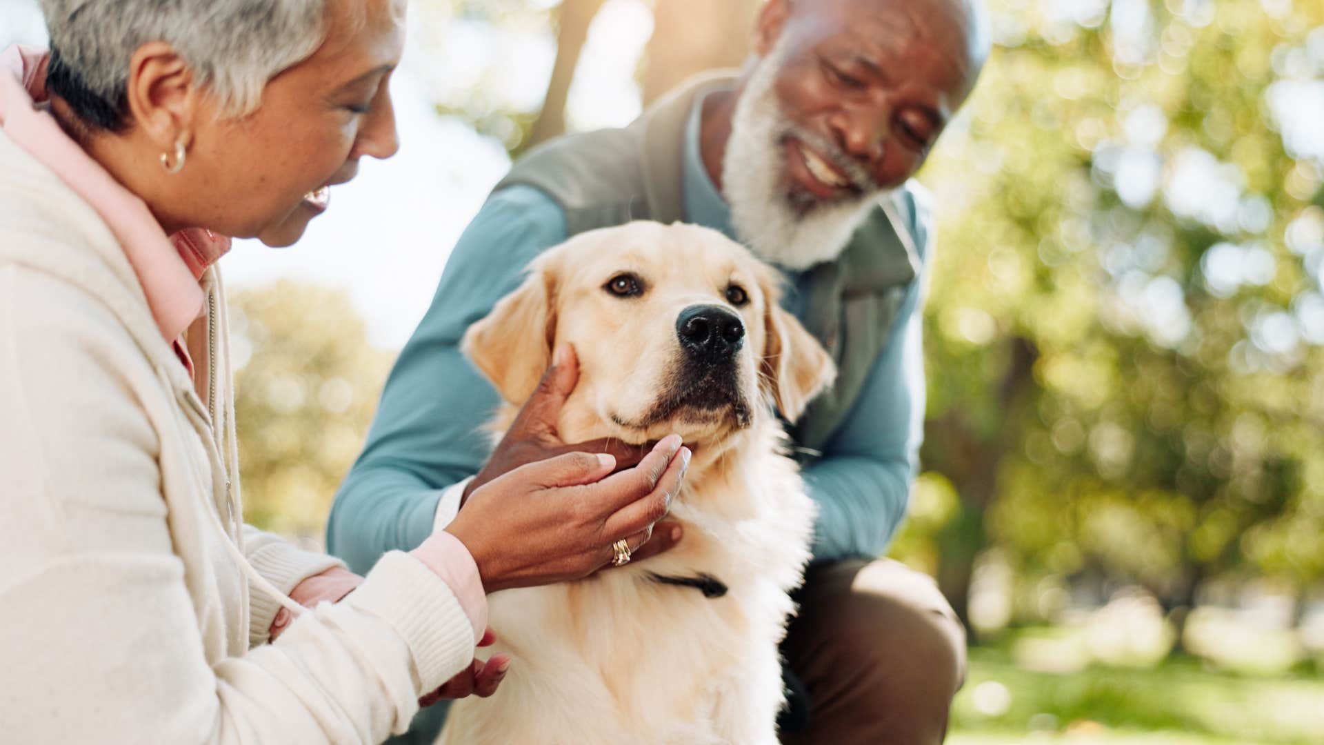 older couple petting their golden retriever outside on a walk