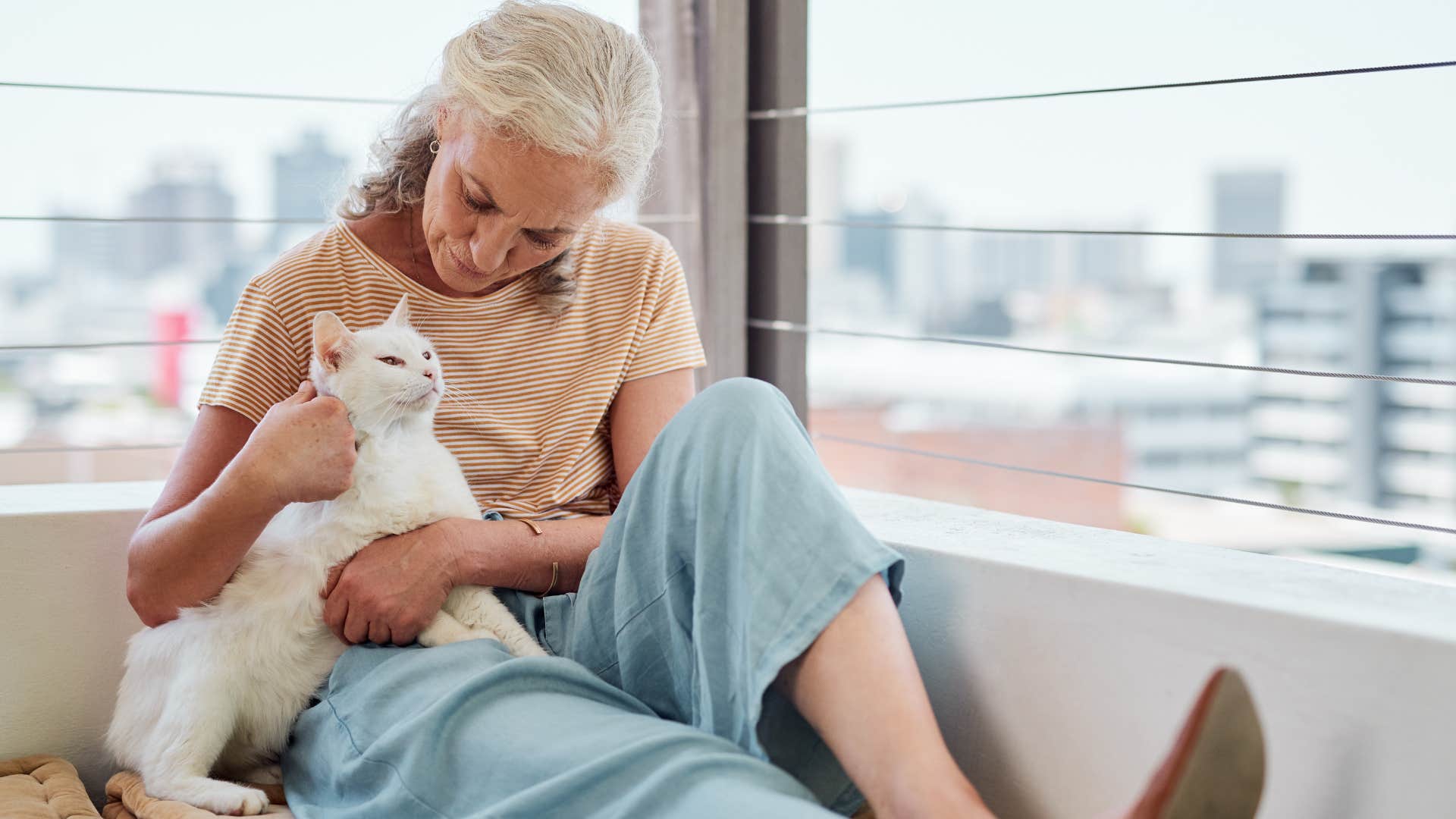 older woman sitting in balcony with her cat making sure it's comfortable