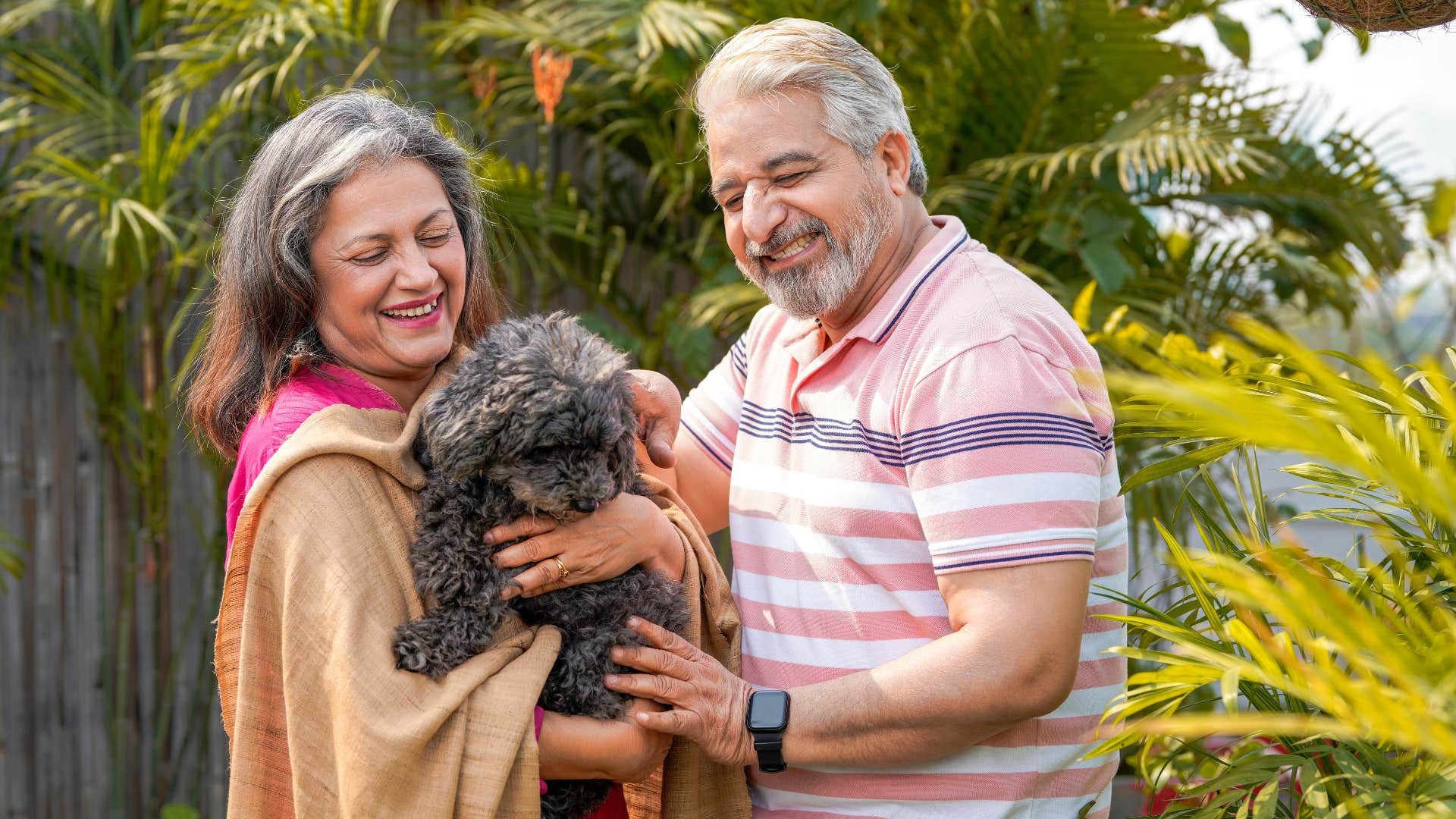 older couple standing outside holding their dog smiling