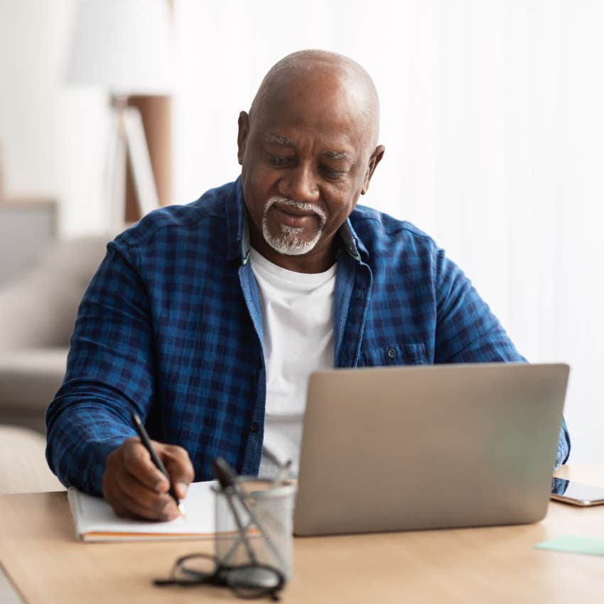 man working on laptop and writing on pad
