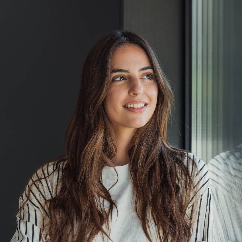 smiling woman looking out window thinking about specific person