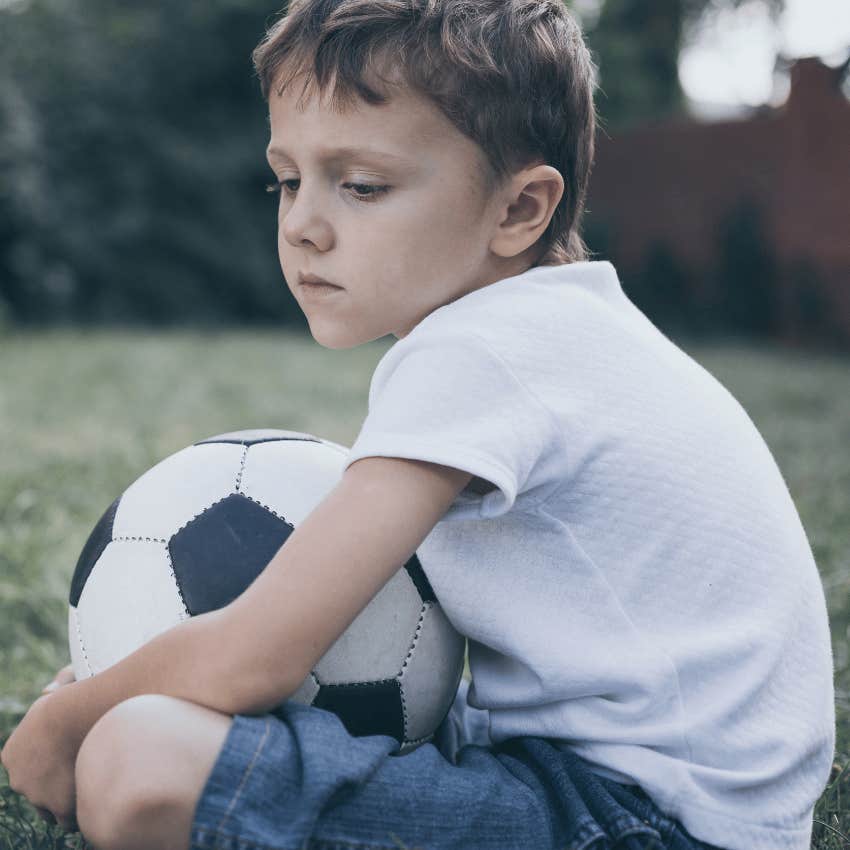 Little boy who had to fend for himself sitting outside with a soccer ball