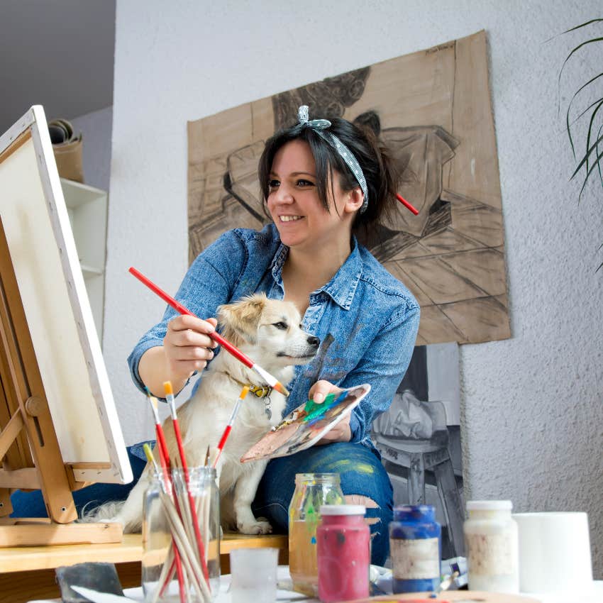 Woman painting with her dog by her side