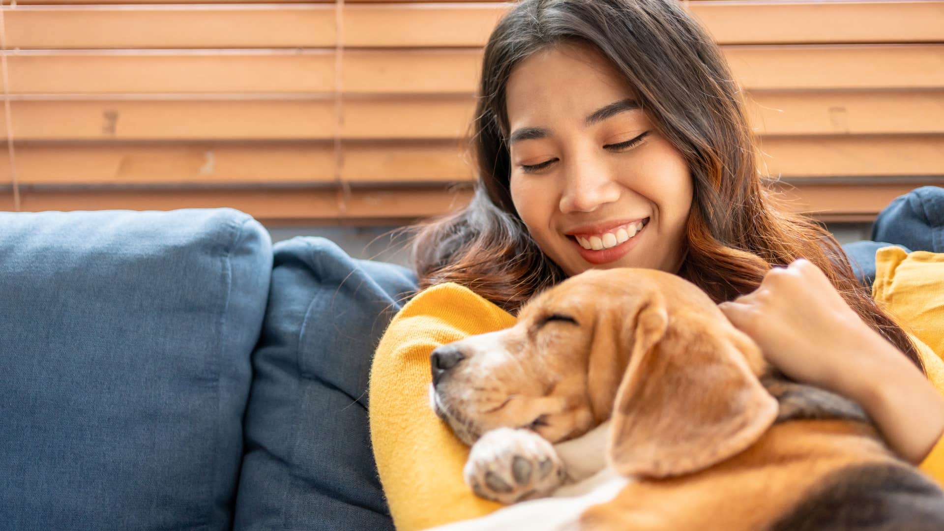 woman interrupting her dog's peaceful time at home by snuggling him