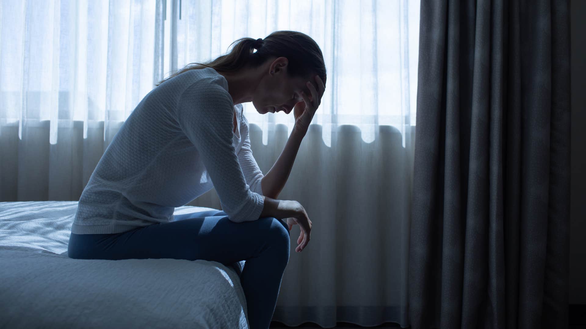 exhausted woman sitting on her bed saying i'm fine i'm just tired