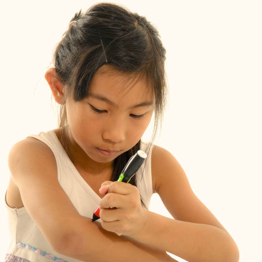 little girl who has heavily tattooed parents drawing tattoos on arm 