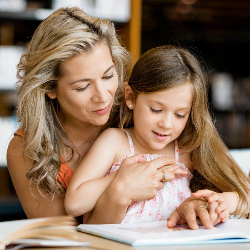 mom sitting with daughter reading book at library
