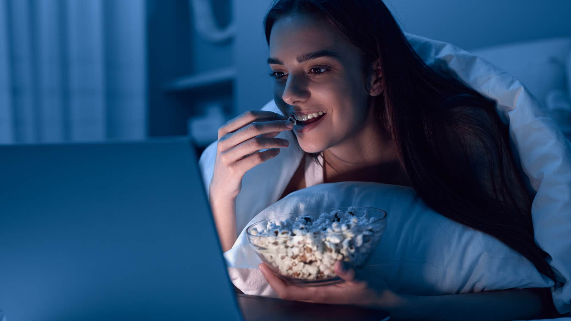 smart woman eating popcorn staying up late watching a movie in bed