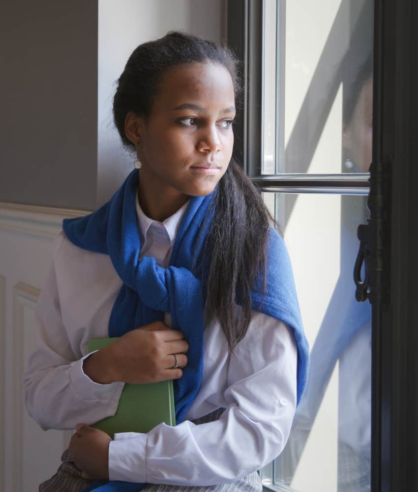 unhappy high school student stares out window with longing