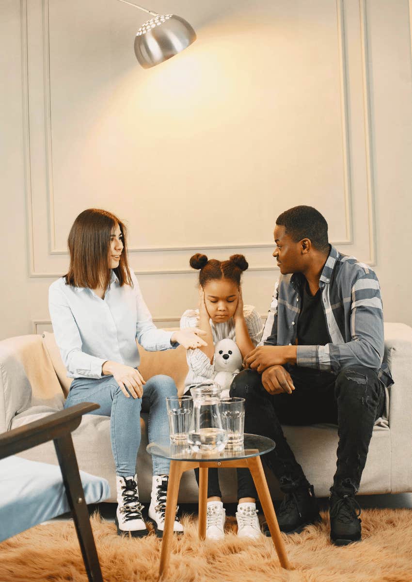 young child covering her ears sitting between her parents