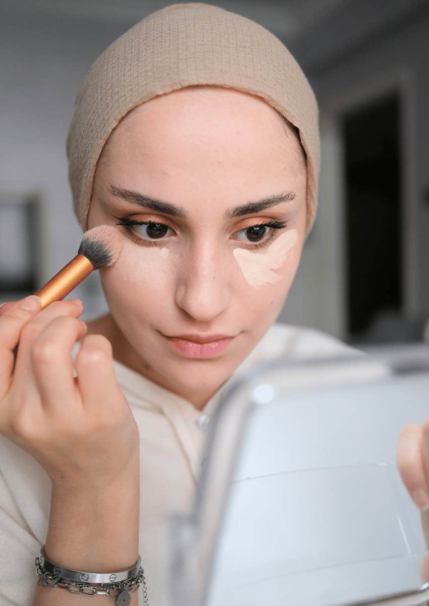 young woman applying concealer under her eyes