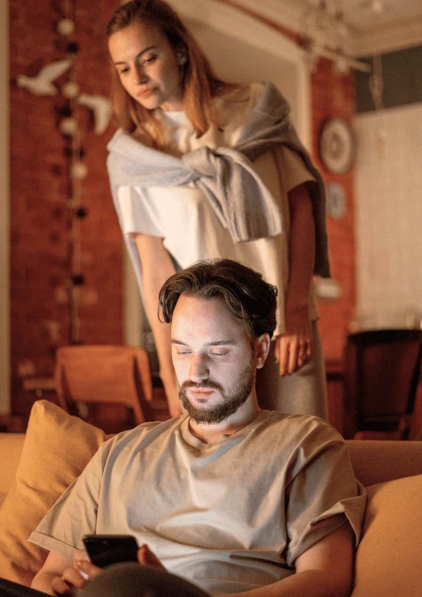 young woman hovering behind man who is on his phone
