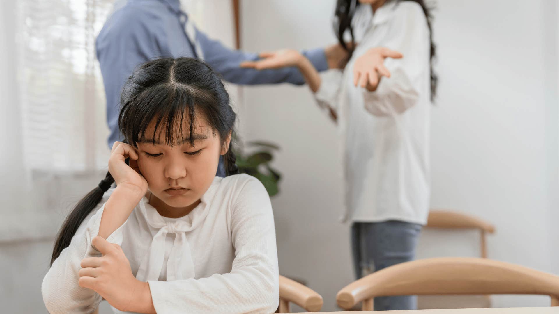 sad little girl sitting near fighting parents