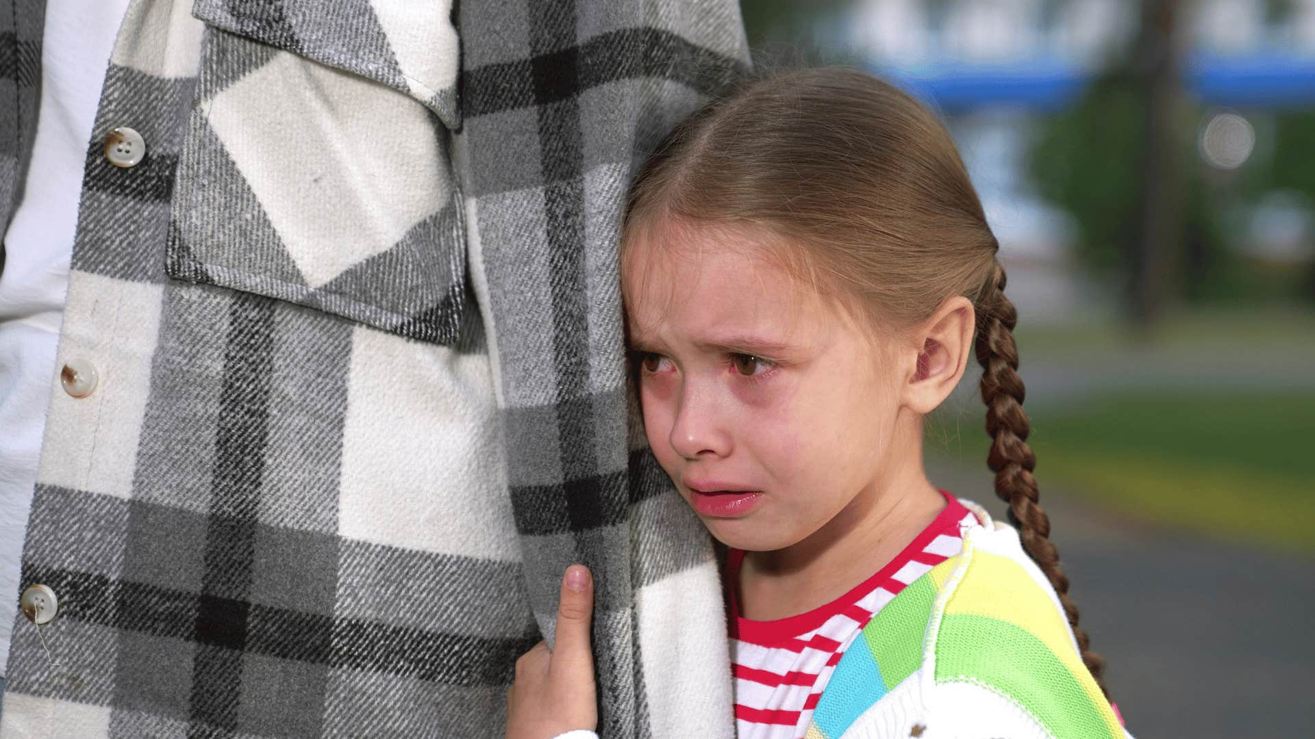 little girl crying experiencing grief holding onto parent's arm