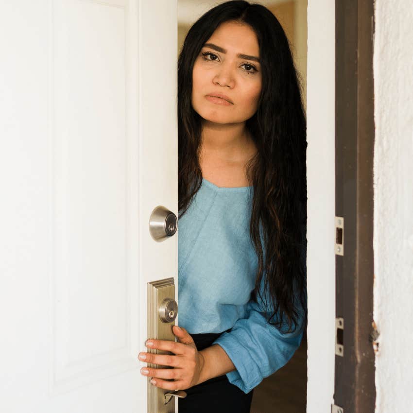 unhappy introverted woman opening the door for uninvited guests at her home