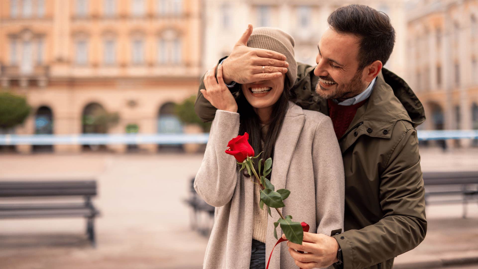 man covering woman's eyes giving her a flower being chivalrous