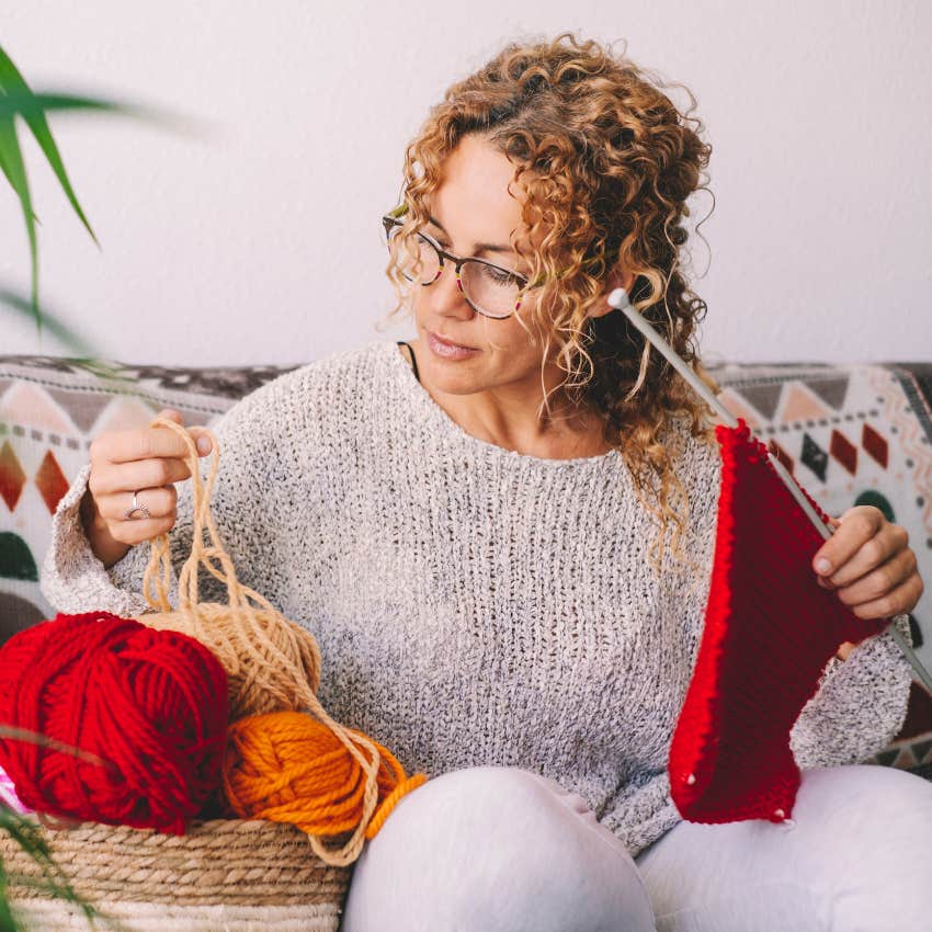 woman sitting on her couch knitting with yarn