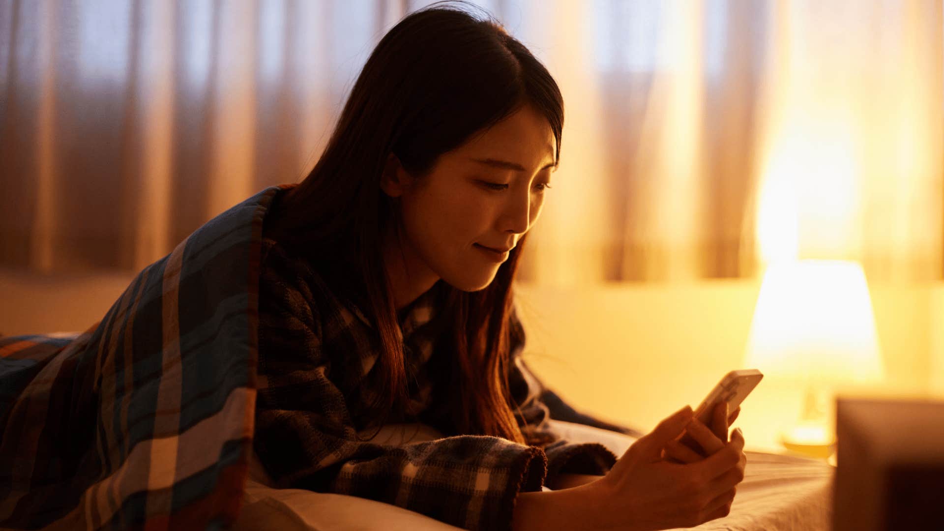woman texting on phone on bed as she has more privacy to reset after a long day