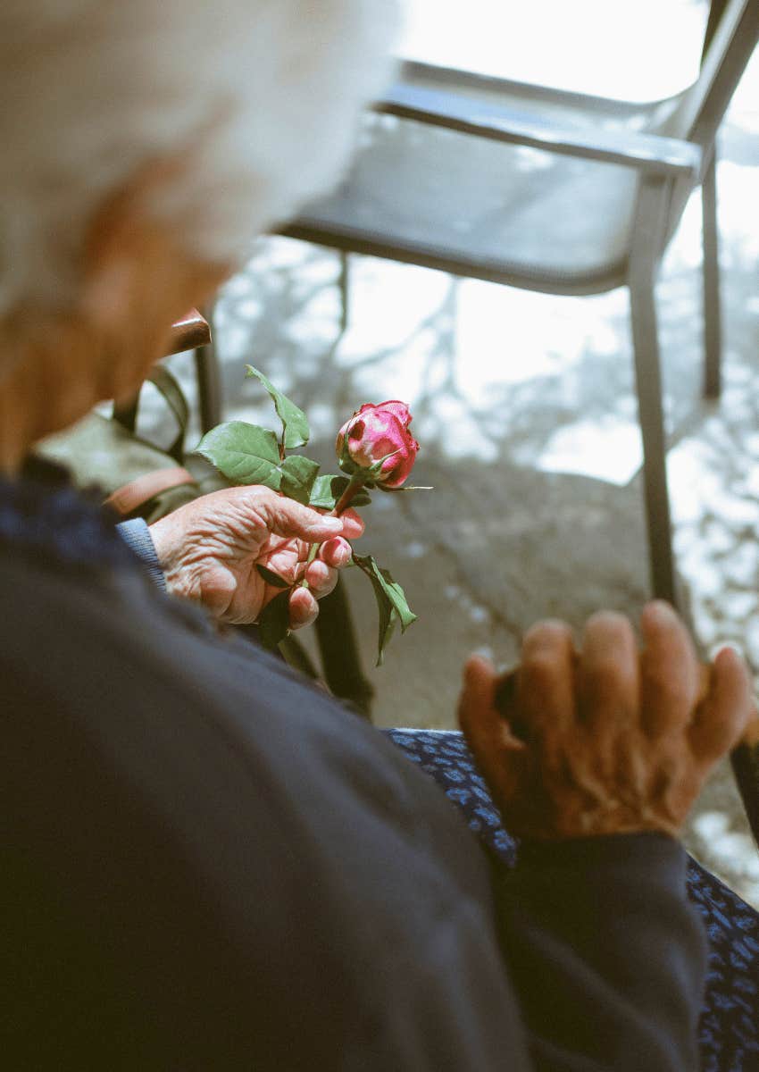 somber older person holding a rose at a funeral